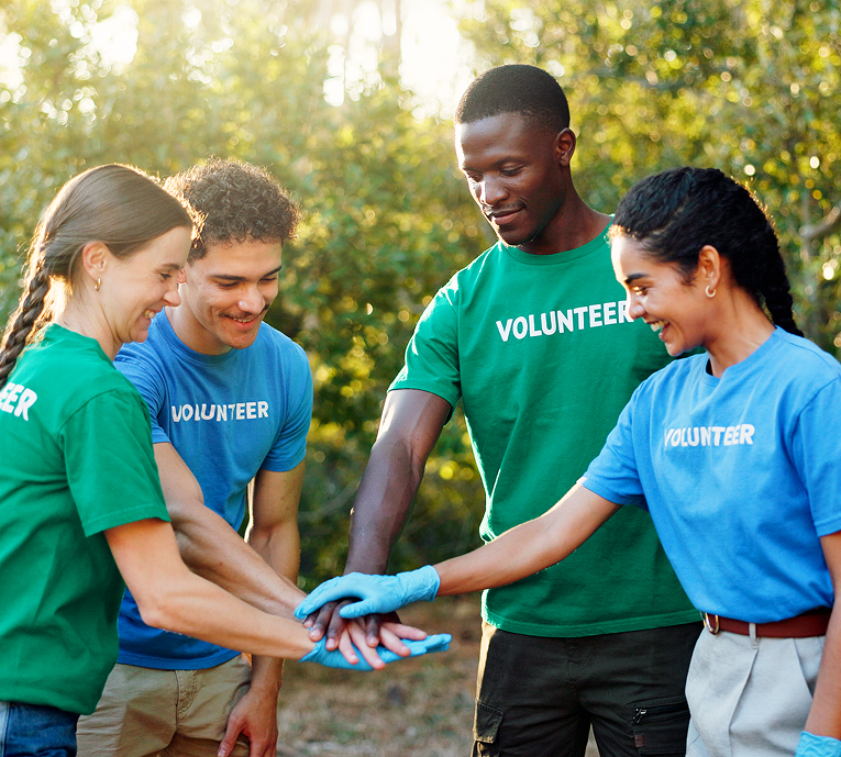 A group of diverse volunteers joining hands outdoors.